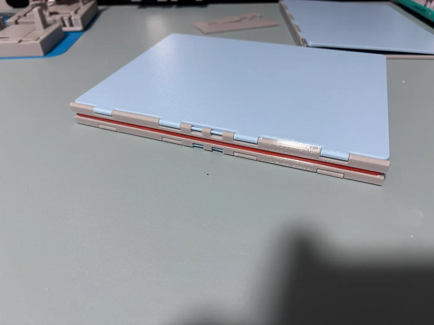 Photograph of the closed blue and grey printed notebook with its spine and red binding band visible.