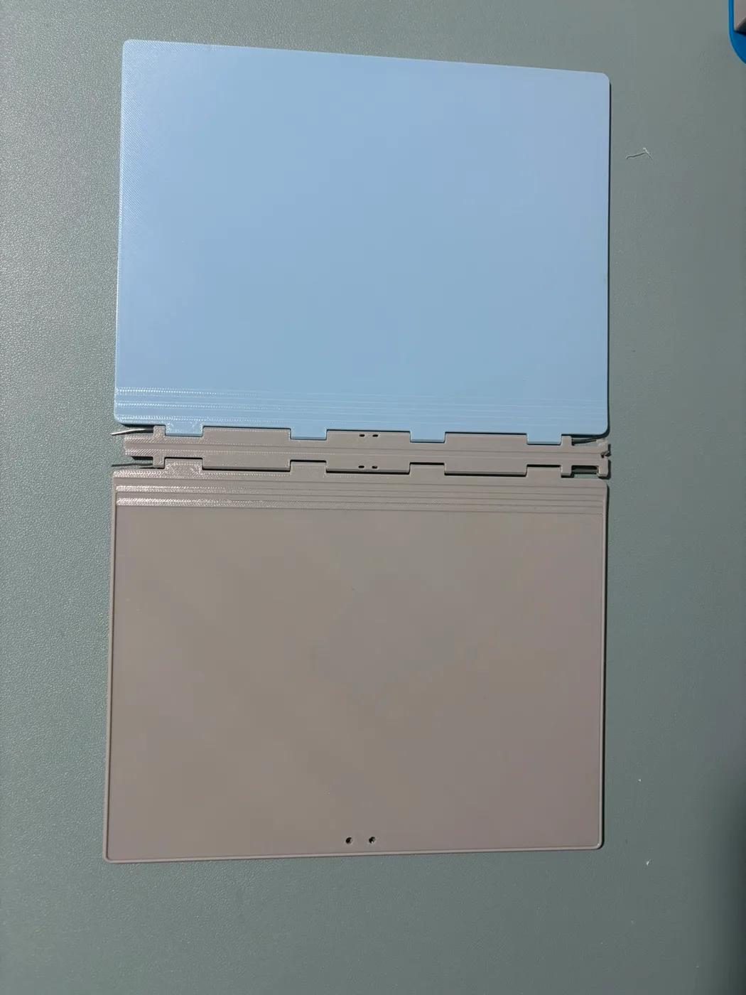 Open blue and grey notebook with paper clips used as hinge pins, broken spine ends on the right, and surviving thin end sections on the left.